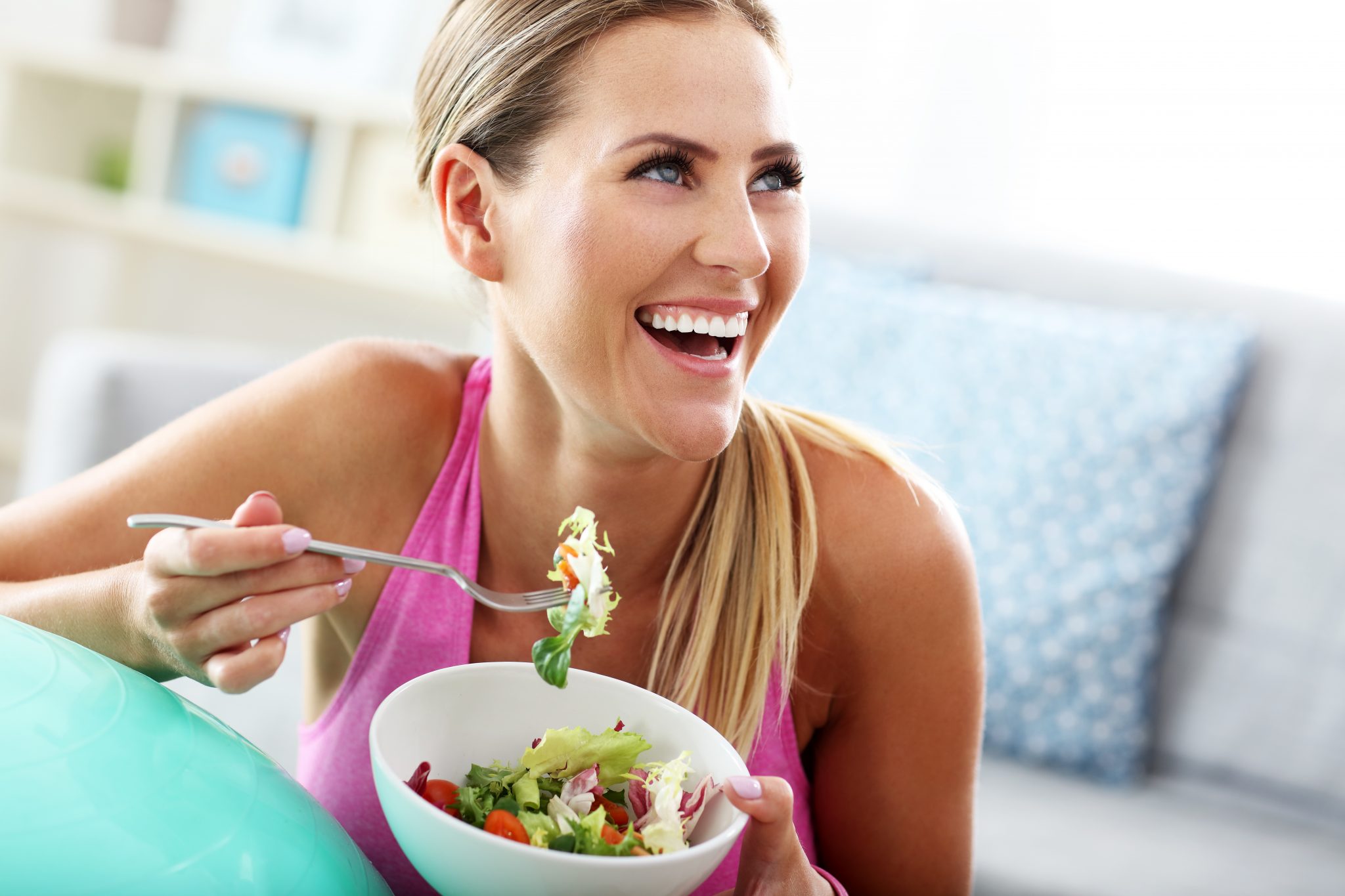 Donna sorridente mangia un'insalata da una ciotola bianca